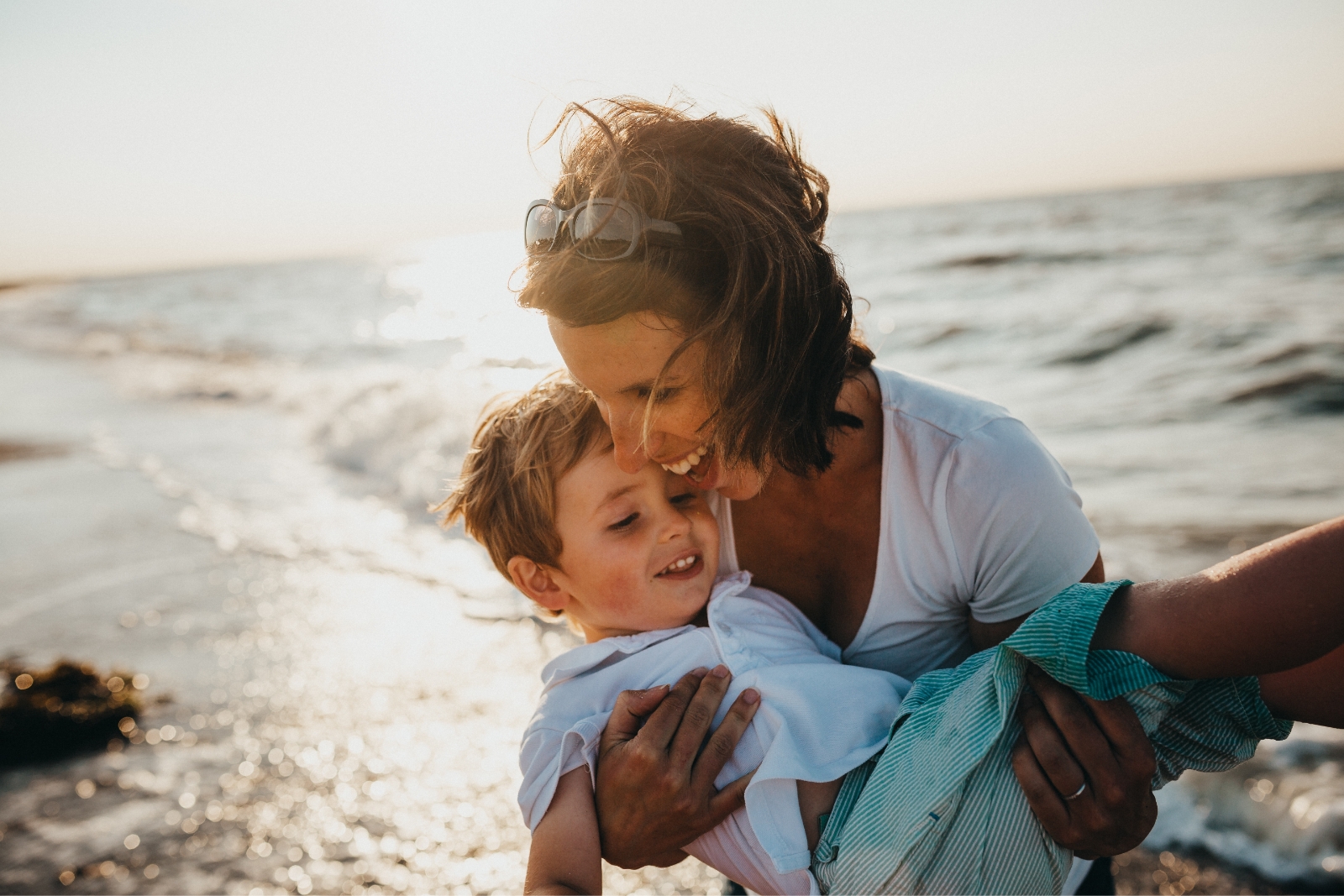 a young boy is being held in his mothers arms, they're at the beach